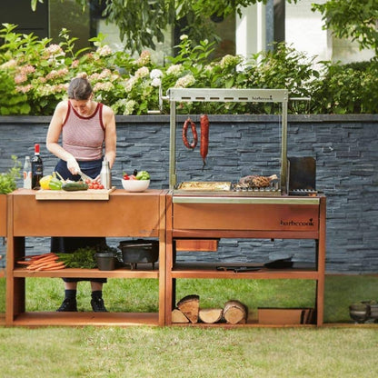 Person preparing food outdoors next to a wooden grill station with vegetables and cooking equipment.